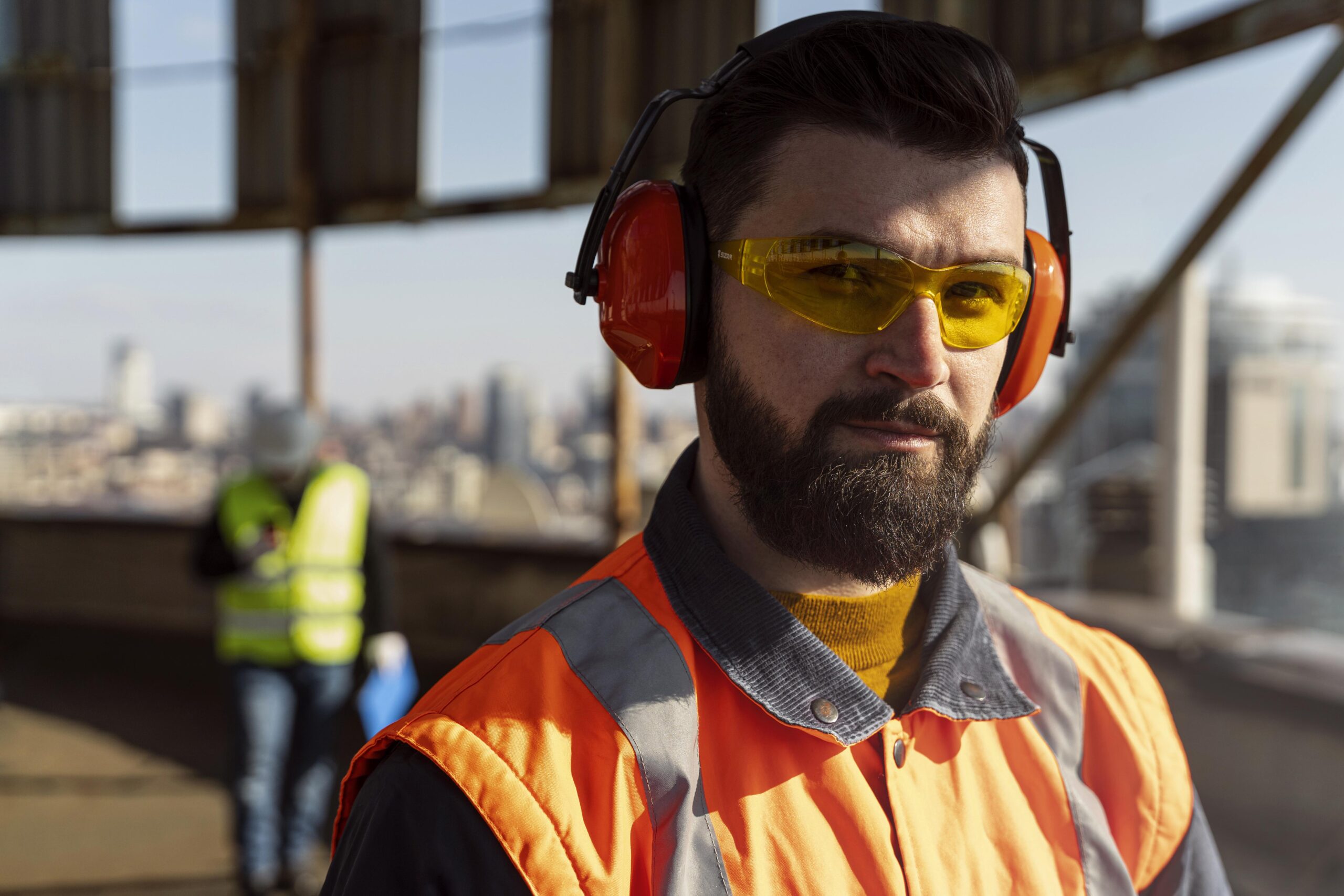 A man in a worksite wearing orange ear protective gear.